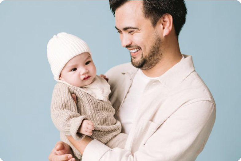 Happy Dad holding his baby.  His baby has a white hat on.
