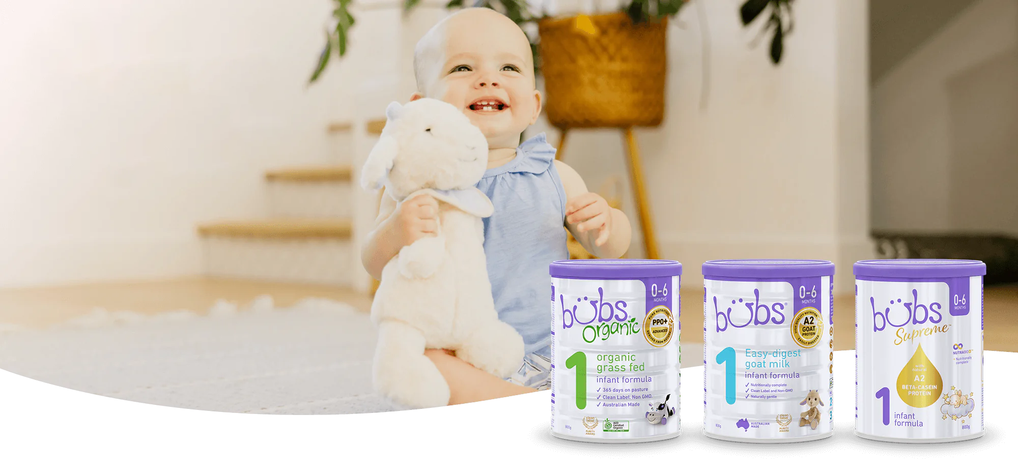 A happy baby with a toy goat and three tins of Bubs Formula