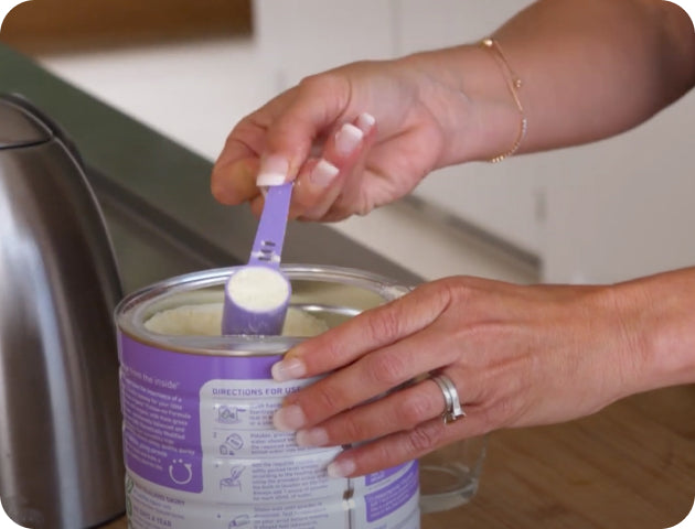 Close-up of a person's hands scooping a serving of formula from a can